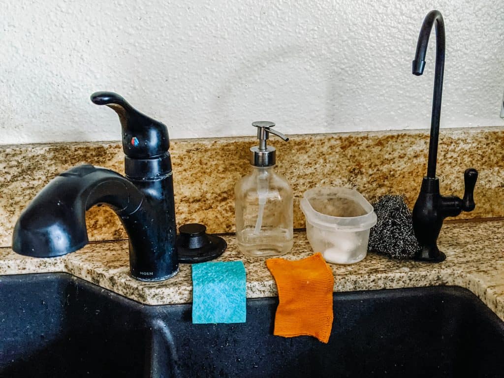 My kitchen sink setup includes several zero waste swaps. A reusable glass soap dispenser, a metal scrubber, and washable cloths instead of paper towels.