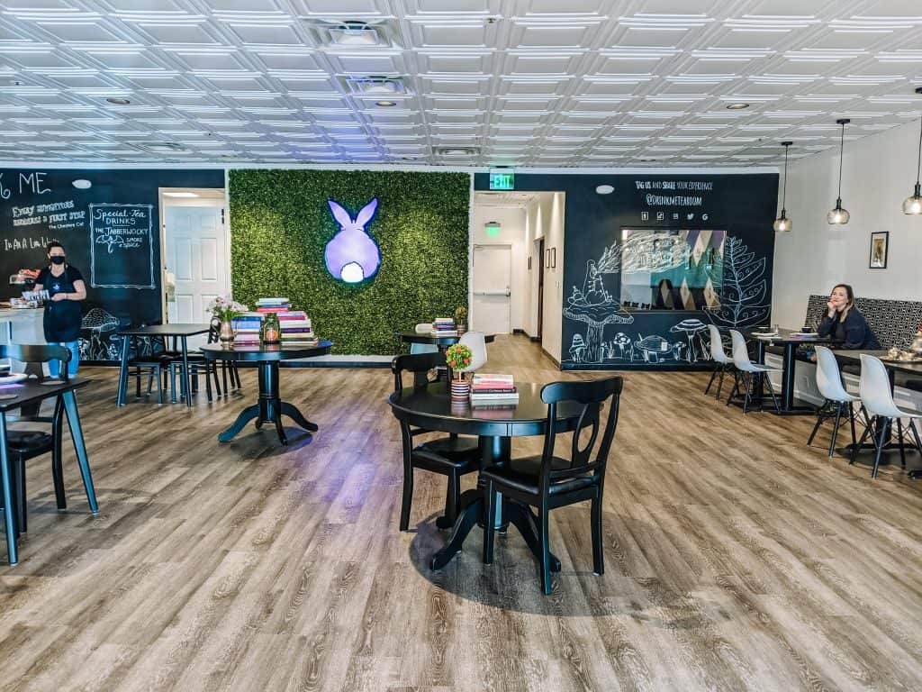 A purple bunny art piece on a green wall. The room features elegant black tables and chairs, cozy seating areas, and charming decor that creates a warm and welcoming atmosphere at Drink Me Tea Room.