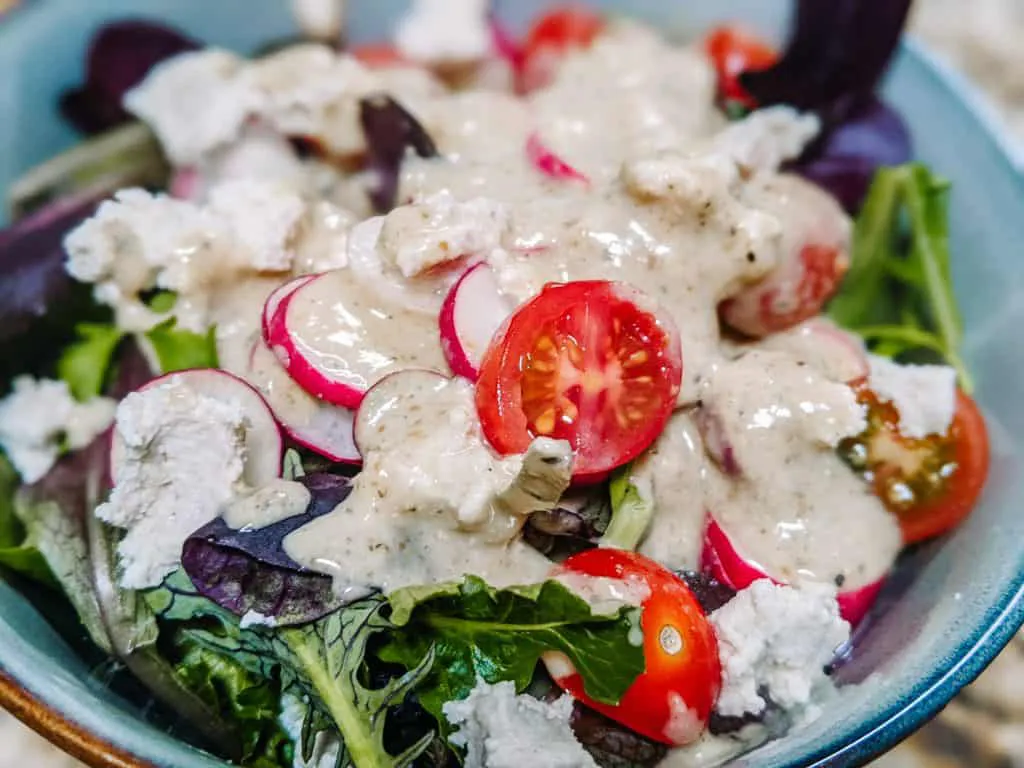 In this bowl, you can see a fresh and colorful salad that's perfect for the best road trip food. It features vibrant cherry tomatoes, crisp radishes, and mixed greens topped with a creamy dressing. This healthy and refreshing salad is easy to pack and makes for a great meal on the go, keeping you energized and satisfied during your travels.