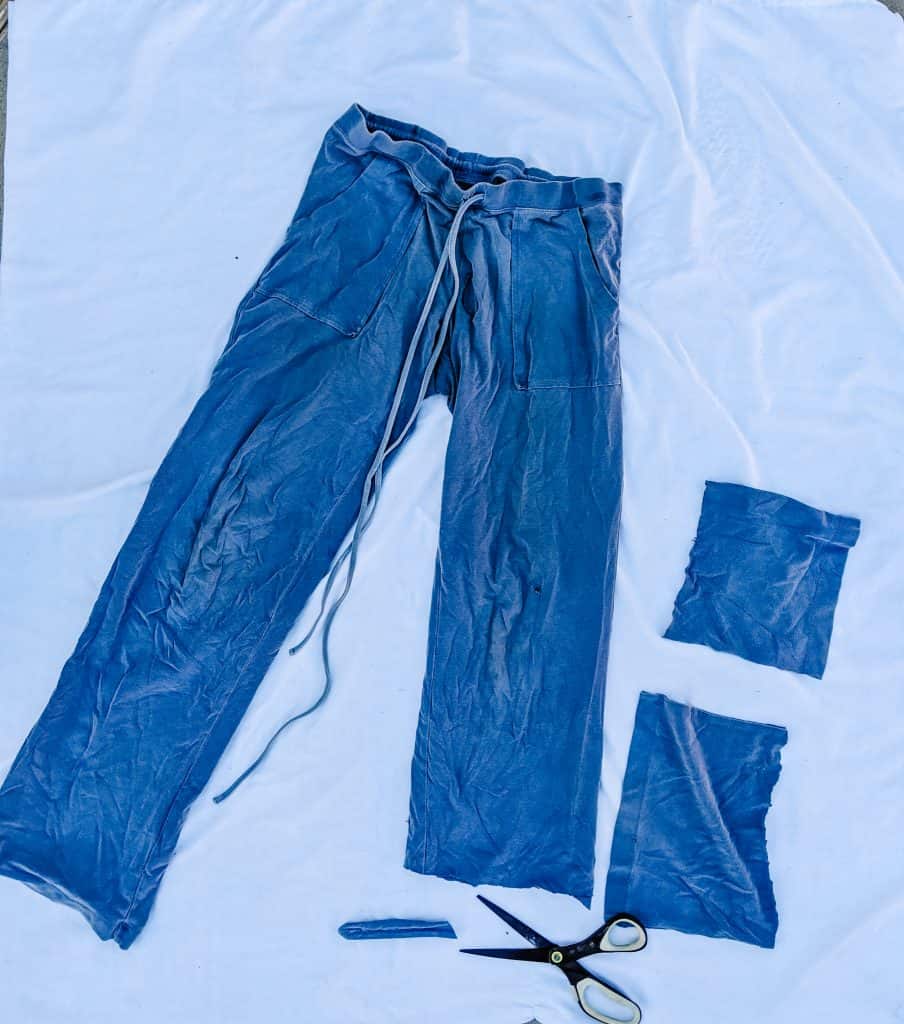 I've laid out an old pair of blue pants on a white surface, ready to be repurposed. I've cut off part of the legs to transform them into rags, which is one of my sustainability examples.