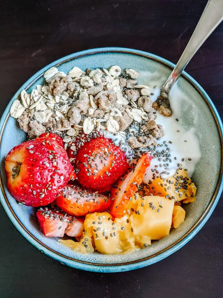 I'm enjoying a bowl of road trip food, perfect for a healthy journey. It's packed with yogurt, fresh strawberries, mango chunks, granola, oats, and chia seeds. It's one of my top choices for PACKING THE BEST ROAD TRIP FOOD, offering a nutritious and delicious start to the day.