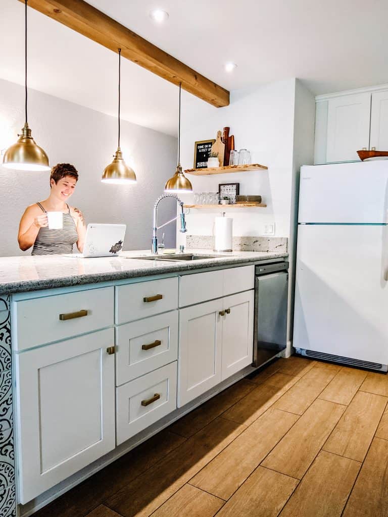 A bright and modern kitchen in the City of Big Bear. The space features white cabinets, a marble countertop, and brass accents on the handles and light fixtures. While I'm enjoying a drink at the island.