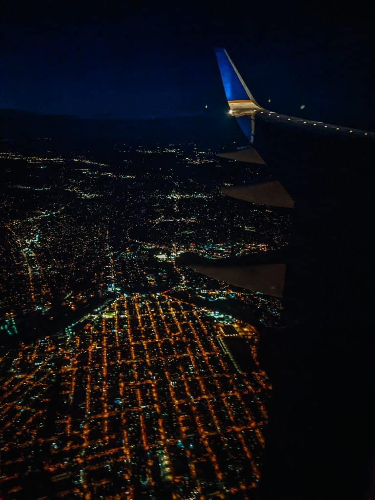 While flying on an airplane at night, I captured this image showing the illuminated city grid below, with the airplane wing visible against the dark sky.