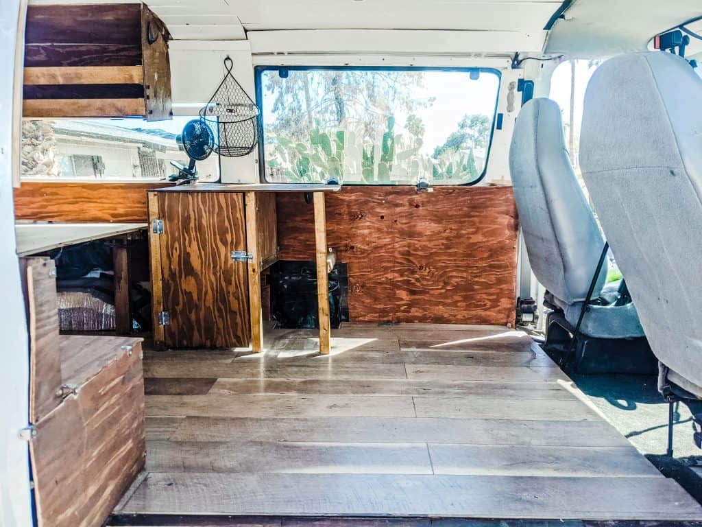 The interior of a Ford camper van features wooden flooring and cabinetry, creating a cozy, rustic atmosphere ideal for road trips.