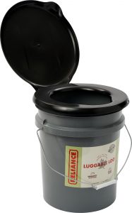 Reliance Luggable Loo, a portable toilet for campervan life. The toilet is essentially a gray bucket with a black plastic seat and lid, which is open. It has a metal handle for easy carrying and is labeled with the product name.