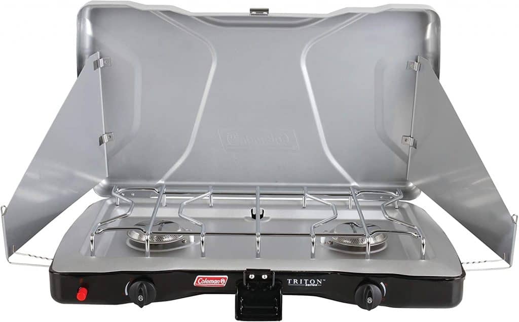 A portable two-burner propane stove, ideal for cooking meals in a camper conversion van, with wind guards on the sides for efficient outdoor cooking.