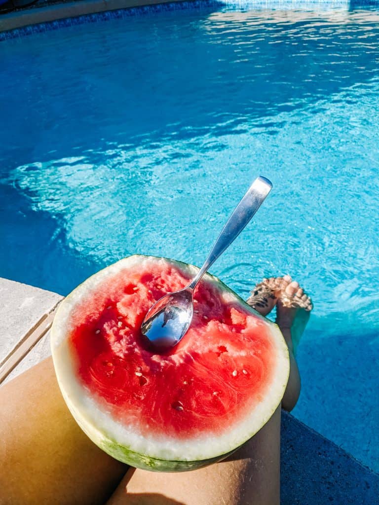 Enjoying a sunny day by the pool in Arizona in winter, eating a fresh watermelon with a spoon while my legs dangle in the water.