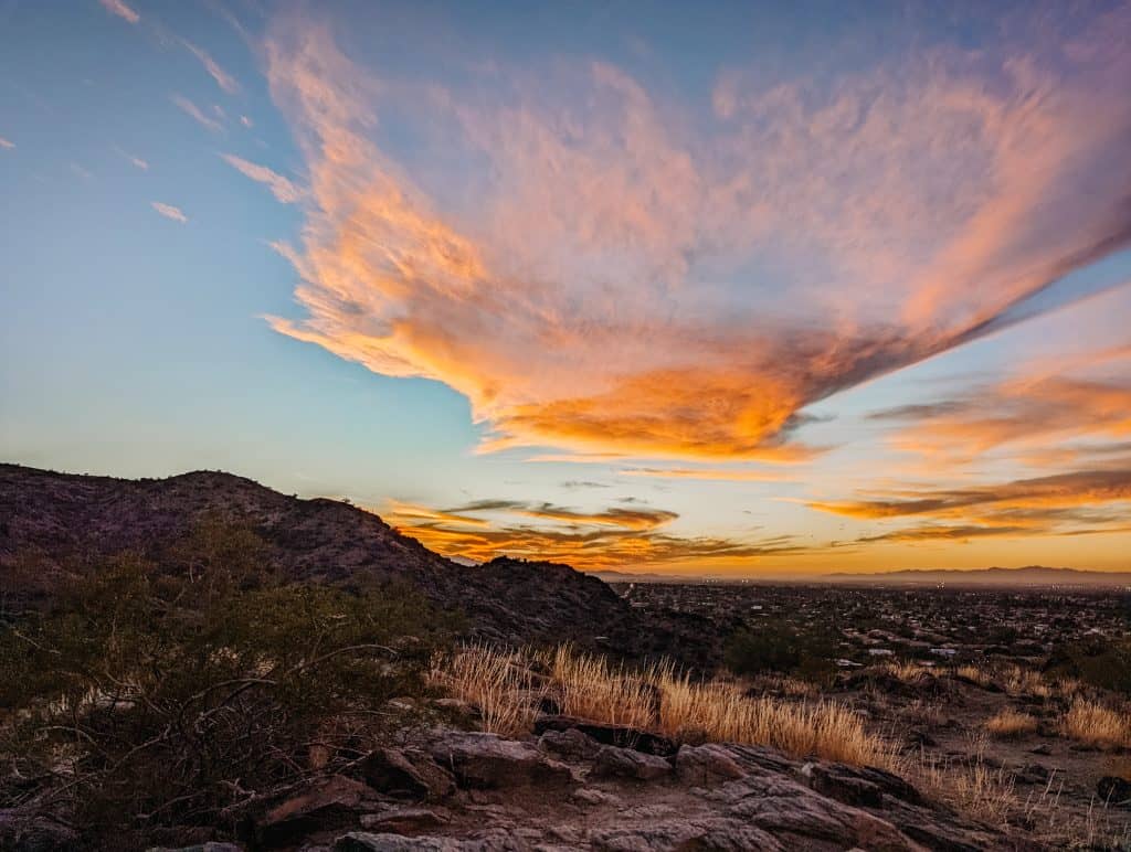 A stunning Arizona in winter sunset with vibrant orange and pink clouds over a rocky desert landscape.