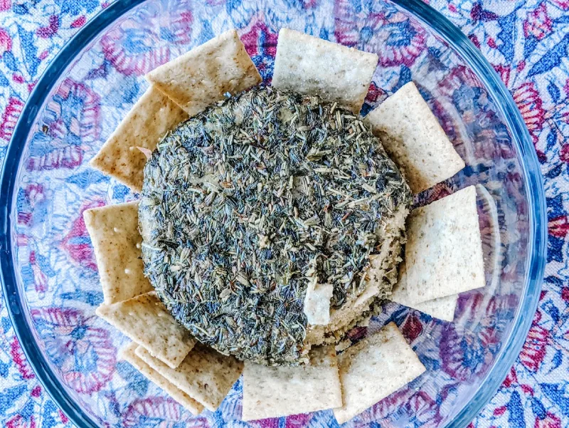 A bowl of herb-covered cheese paired with crispy crackers. This combination is a tasty and convenient option for munching on the go, making it one of the best road trip foods you can pack.