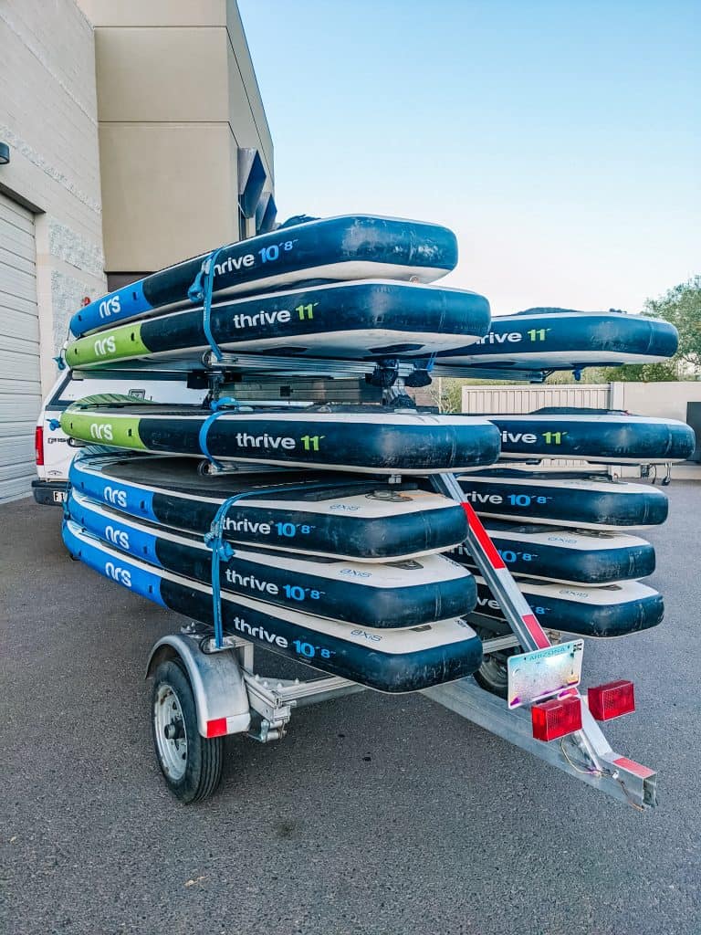 A trailer loaded with multiple paddleboards stacked neatly, ready for transport, as part of the equipment for an adventure guide.