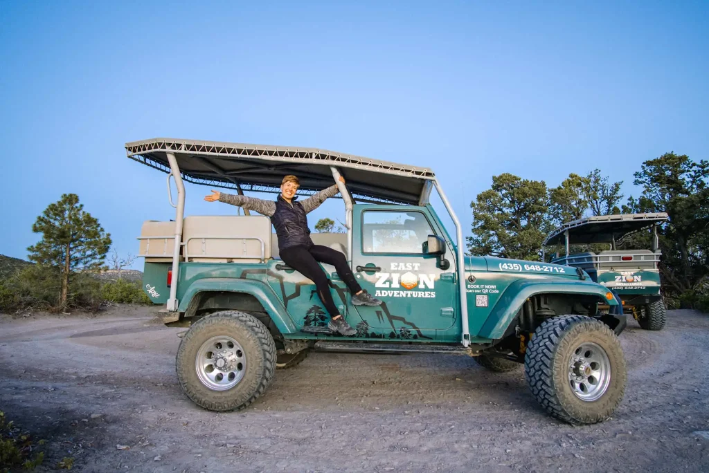 I am sitting on the side of a green jeep with "East Zion Adventures" written on it, enjoying an exciting outdoor adventure at Zion Ponderosa Ranch Resort.