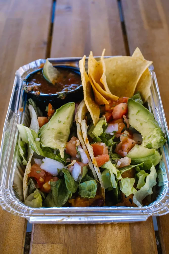 A close-up view of a fresh taco platter with avocado slices, tomatoes, lettuce, and salsa from Kiki Dee's Taqueria at Zion Ponderosa Ranch Resort.