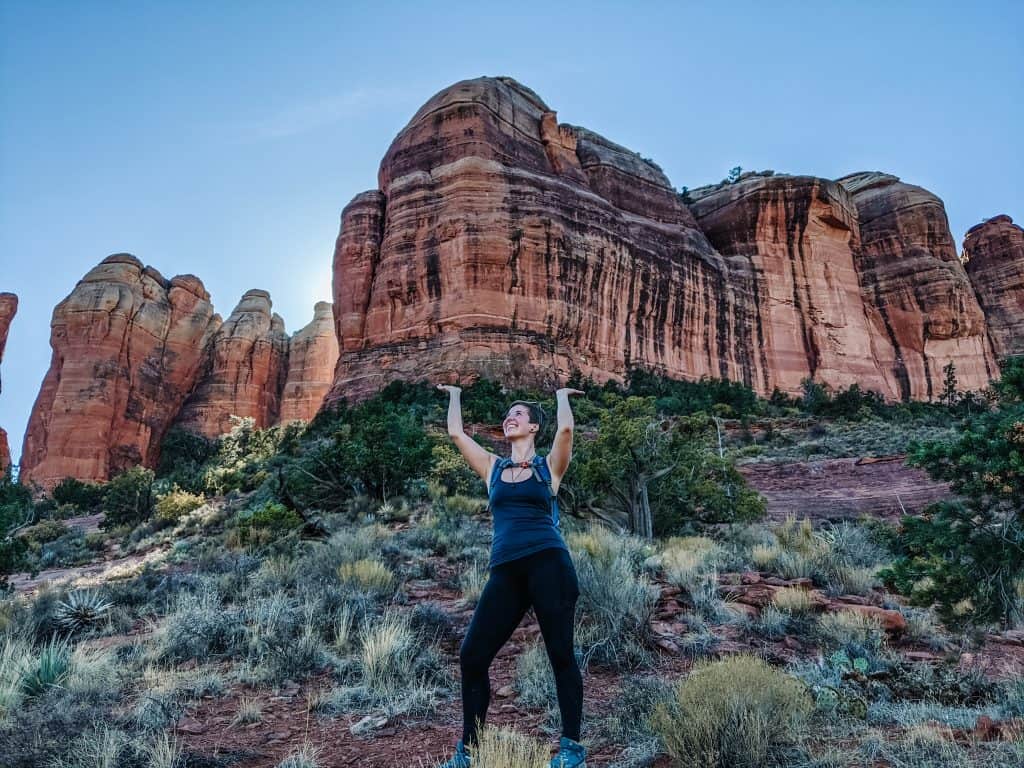 I am standing with my arms raised in front of the towering red rock formations of Sedona, with the clear blue sky overhead. The keyword "Sedona vortex" naturally comes to mind as this location is famous for its energy vortices.