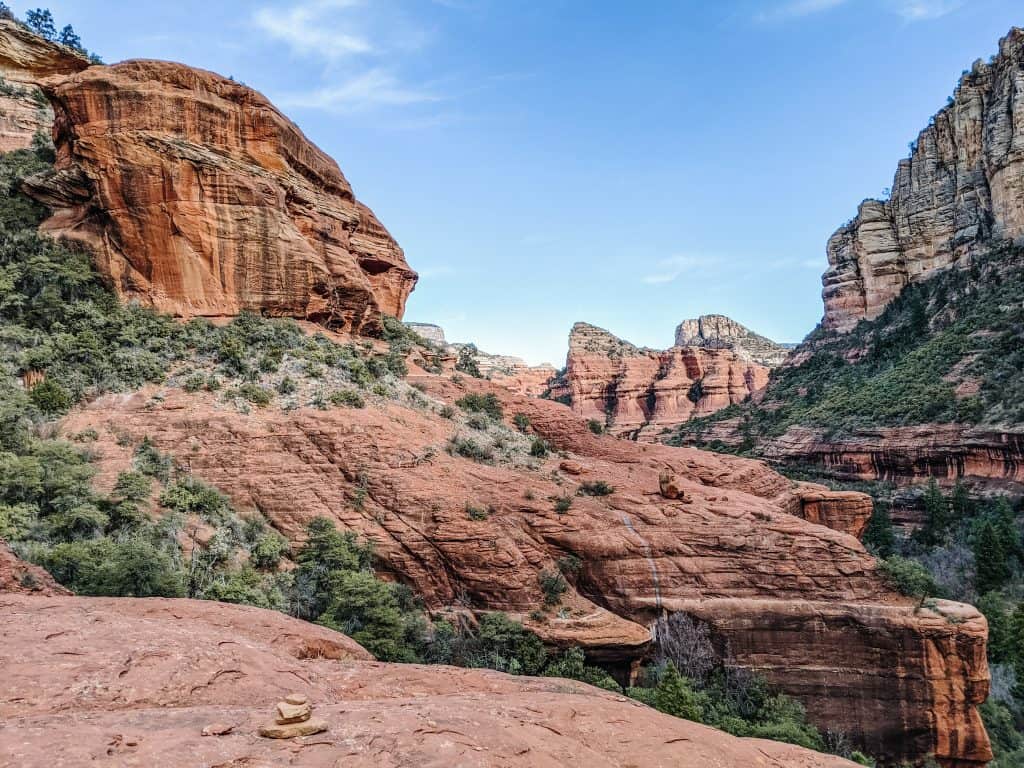 The stunning red rock formations of the Sedona vortex, with layered cliffs and green vegetation under a clear blue sky, capturing the natural beauty and unique landscape of Sedona.