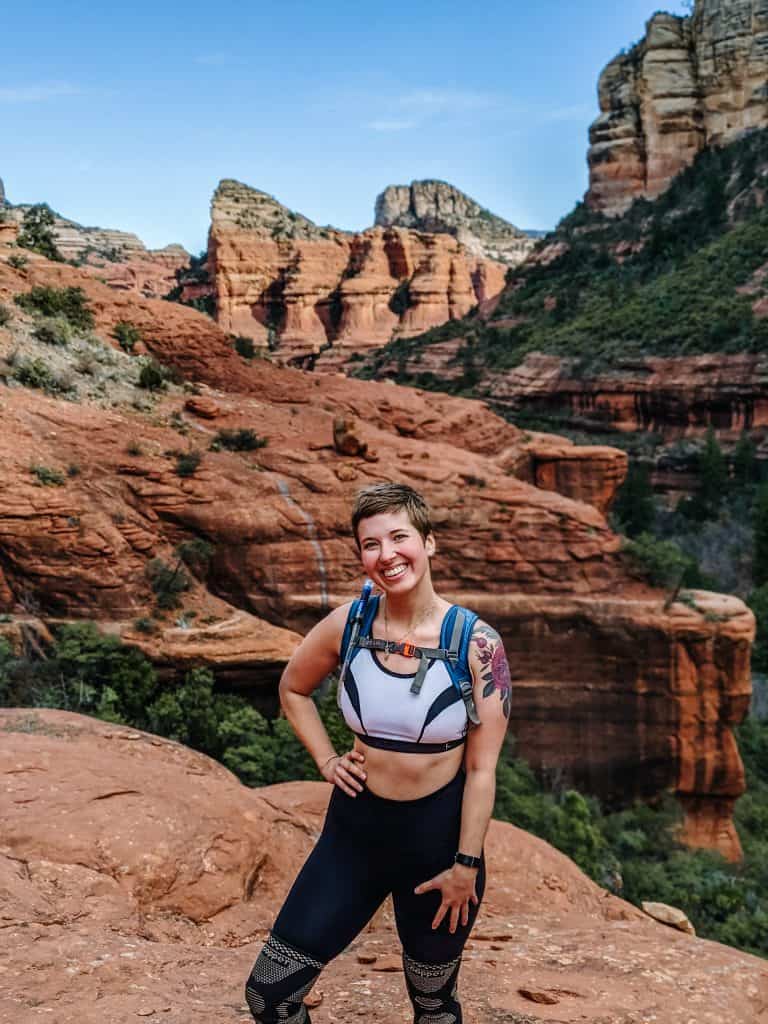 I'm standing on a red rock formation in Sedona, with the stunning landscape of the Sedona vortex in the background. The red rocks and the greenery below highlight the unique beauty of this area. The clear blue sky enhances the breathtaking scenery, making this hike in Sedona a memorable experience.