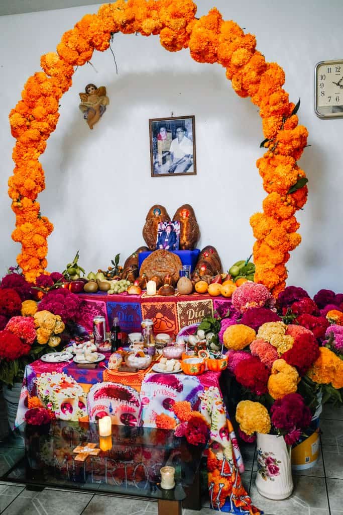 A colorful Day of the Dead Mexico altar adorned with marigold arches, photos, candles, and various offerings, honoring deceased loved ones.