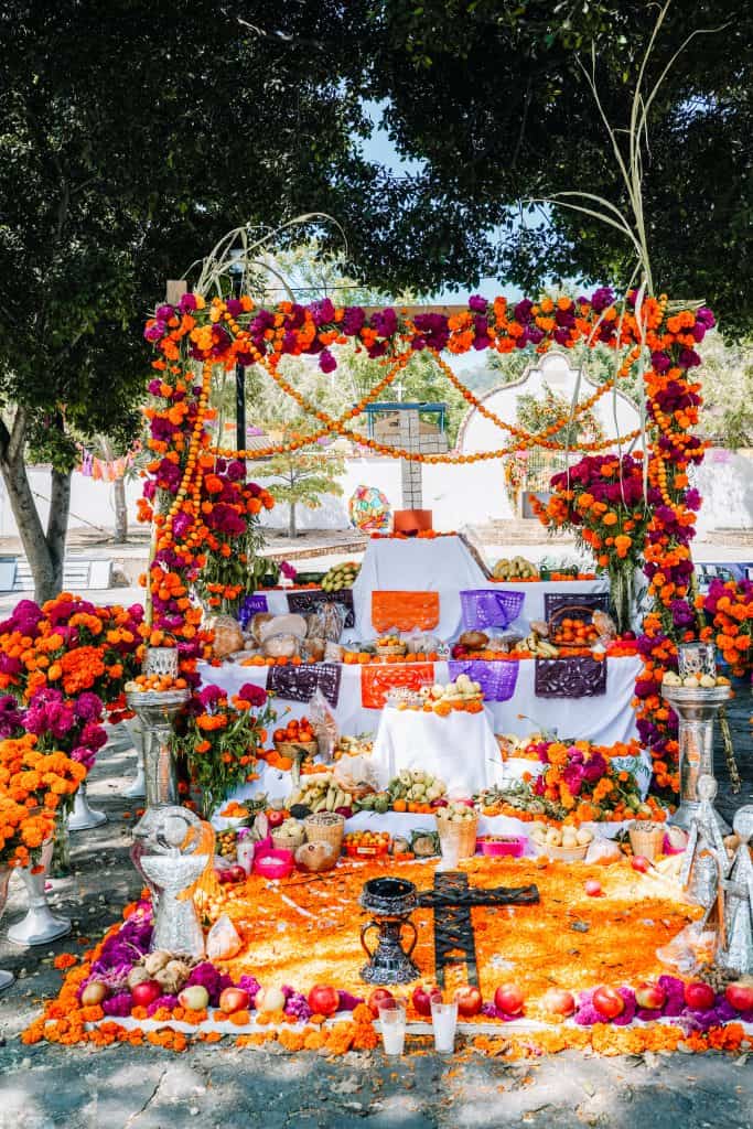 A vibrant and elaborate altar set up outdoors for the Day of the Dead in Mexico, adorned with colorful marigolds, candles, and various offerings to honor the deceased.