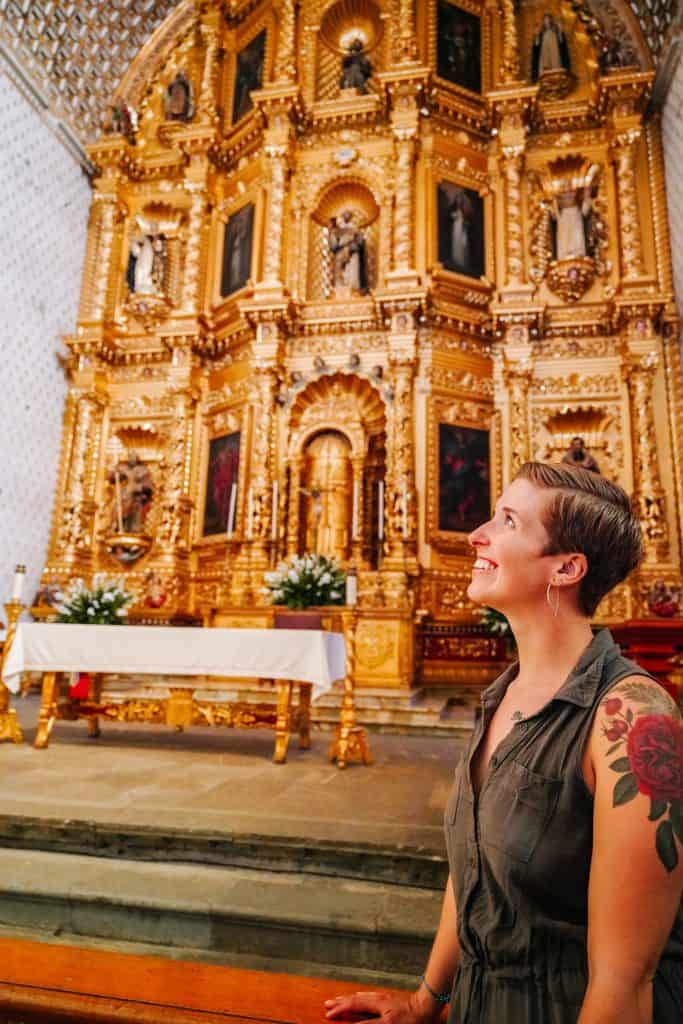 Standing inside a beautifully ornate church in Mexico, gazing up at an elaborately gilded altar adorned with religious statues and carvings. This sacred space is particularly significant during the Day of the Dead Mexico