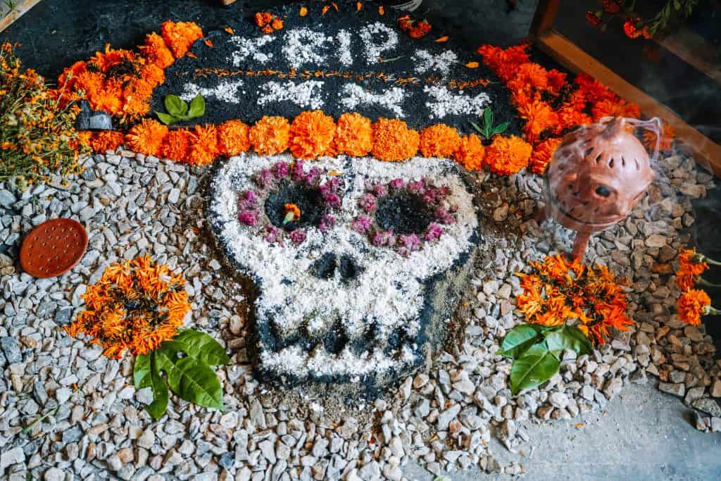 A Day of the Dead altar in Mexico with a decorative skull made from colored sand and surrounded by marigold flowers, signifying remembrance and honoring deceased loved ones.