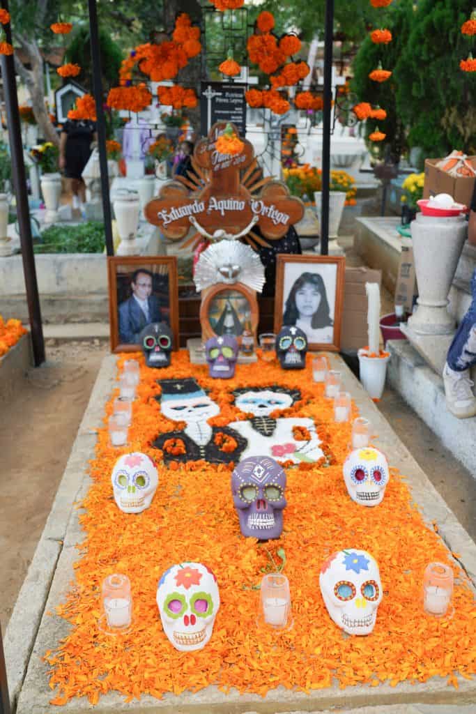 A grave decorated for the Day of the Dead in Mexico. The grave is adorned with bright orange marigold petals, colorful sugar skulls, candles, and photographs of the deceased.