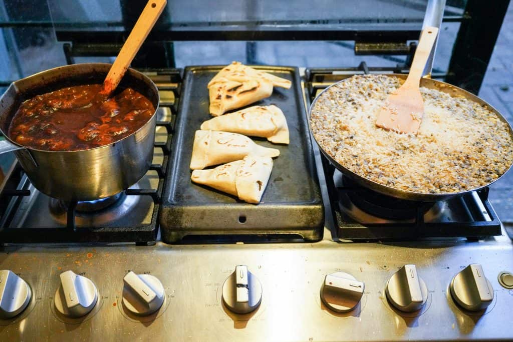 A bustling Oaxaca restaurant kitchen with a pot of rich stew simmering on the stove, alongside perfectly folded quesadillas cooking on a griddle, and a pan filled with a creamy sauce, capturing the essence of traditional Mexican cooking.