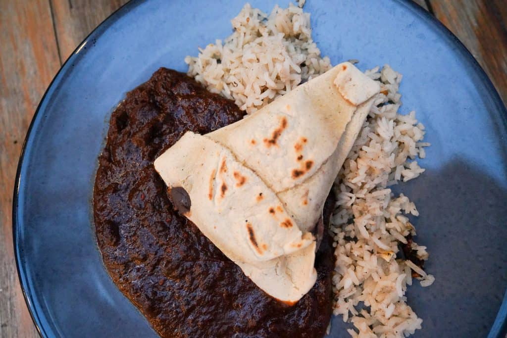 A plate from an Oaxaca restaurant features a rich, dark mole sauce spread over rice, accompanied by a folded, lightly toasted tortilla, capturing the essence of traditional Mexican cuisine.