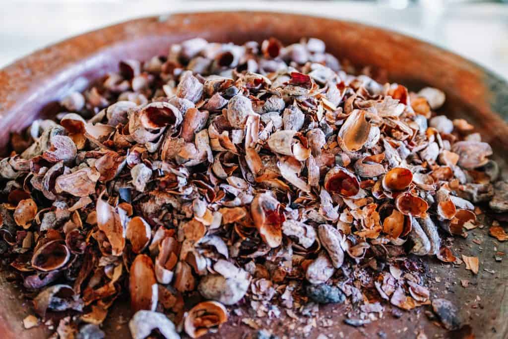 A wooden plate filled with the broken shells of peeled cacao beans, illustrating the meticulous and traditional preparation process often seen in a Oaxaca restaurant.