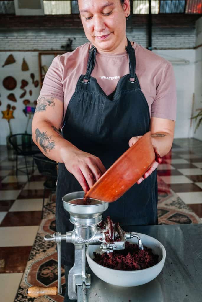 A person at an Oaxaca restaurant is seen grinding roasted cacao beans using a traditional hand-crank grinder, highlighting the authentic preparation methods used in Oaxacan cuisine.