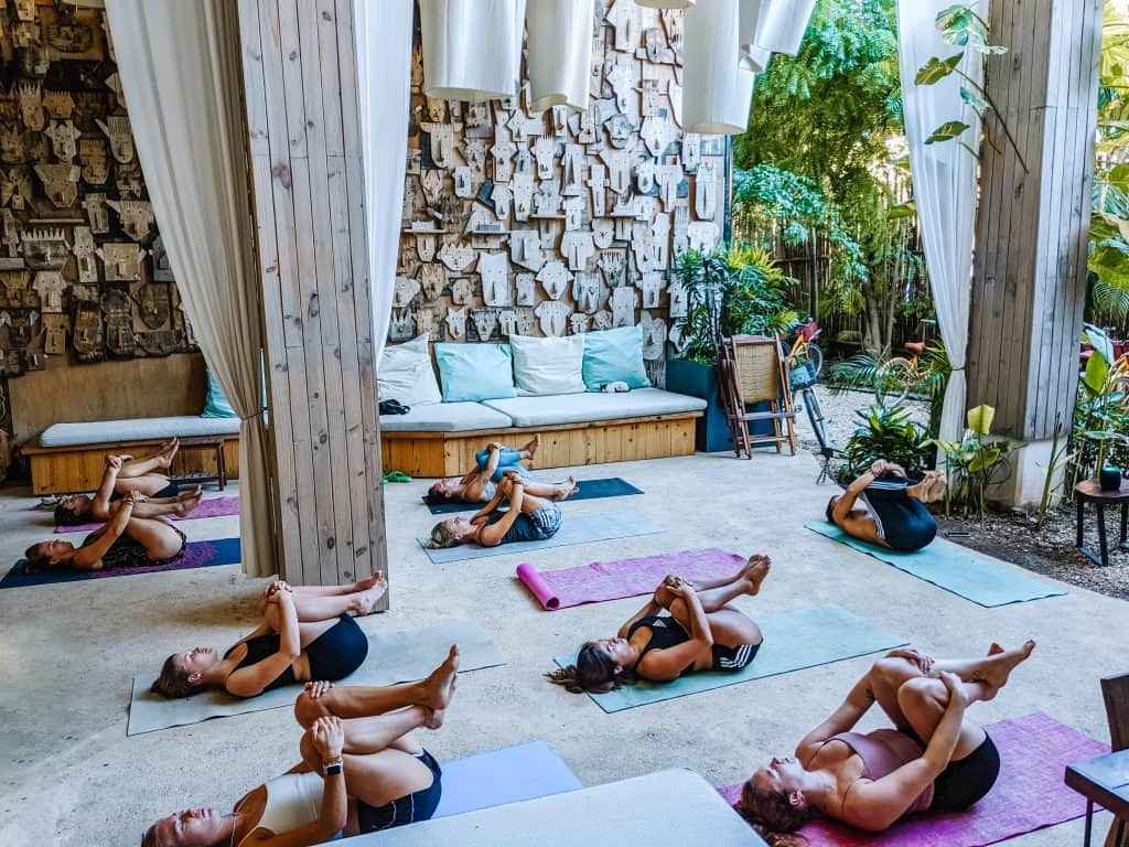 A group of people practicing yoga in an outdoor studio with wooden pillars and lush greenery, highlighting the importance of incorporating relaxation techniques when learning how to recover from burnout.