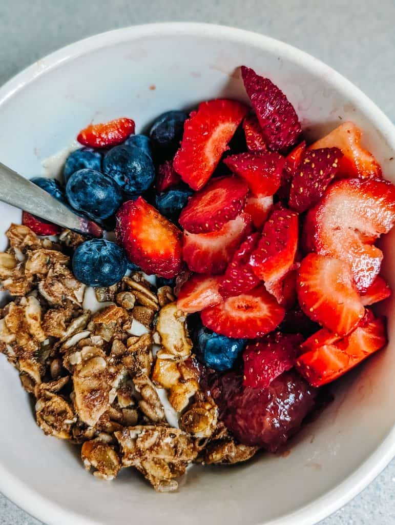 A bowl filled with fresh strawberries, blueberries, granola, and a spoon, perfect for a nutritious breakfast, is shown. Eating a balanced diet, like this bowl of berries and granola, is a crucial step in learning how to recover from burnout.