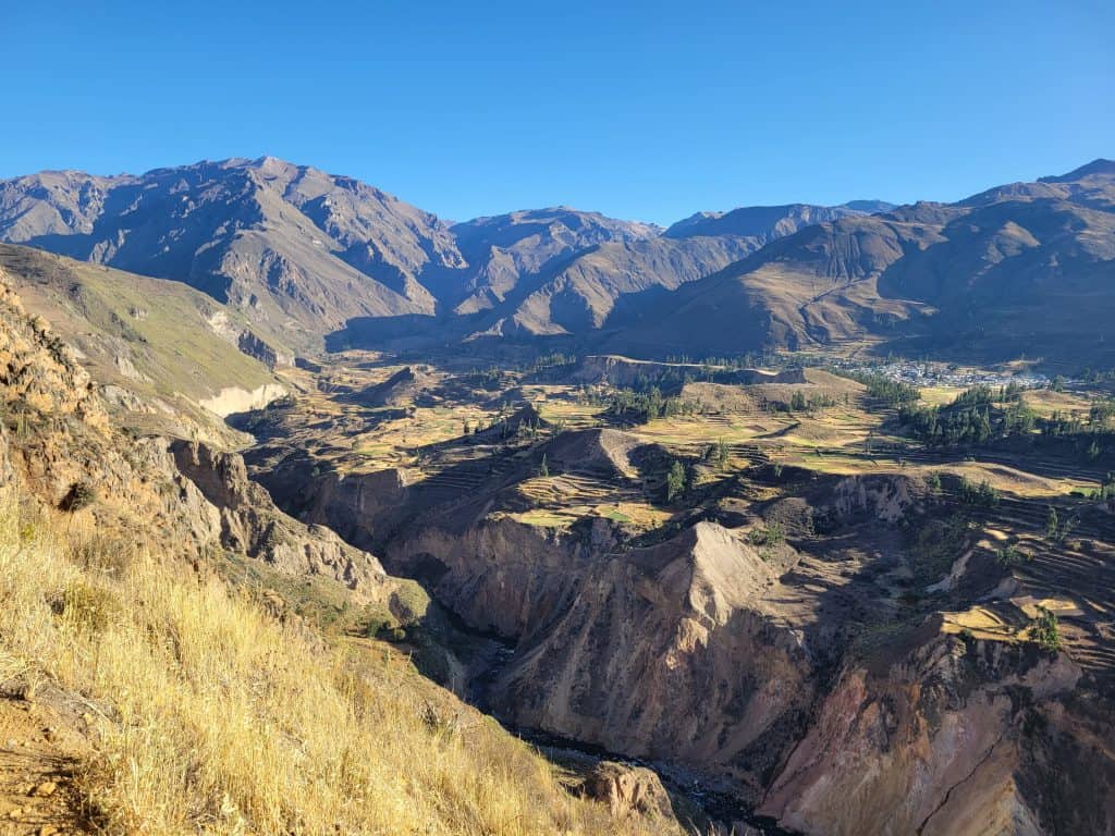 The majestic Colca Canyon in Peru, one of the deepest canyons in the world. The landscape is marked by steep, rugged cliffs and terraced agricultural fields stretching into the distance, with towering mountains providing a dramatic backdrop.