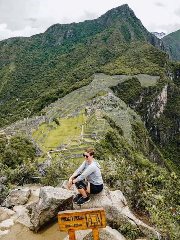 Here I am sitting on a rock at Machu Picchu, with the sprawling ancient ruins and terraced fields stretching out behind me. One of the top things to do at Machu Picchu is to hike up to these viewpoints for a panoramic view of the historical site and the surrounding lush mountains.