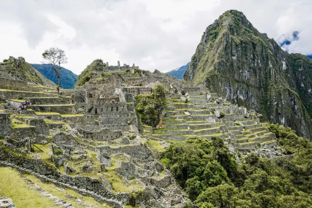 The iconic ruins of Machu Picchu, surrounded by green mountains. The ancient Incan city features terraced fields and stone structures against the backdrop of the towering Huayna Picchu peak. Exploring these historic ruins is one of the top things to do at Machu Picchu.