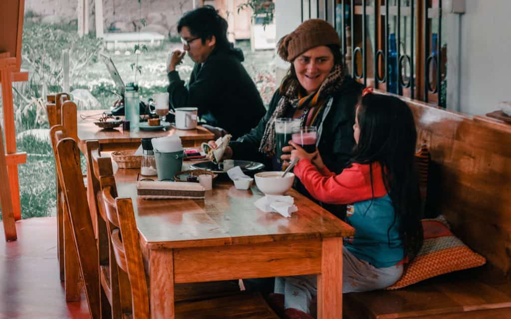 A mother and her child enjoy a meal together at a cozy vegan restaurant in Sacred Valley, Peru, sitting at a wooden table with warm, inviting surroundings.