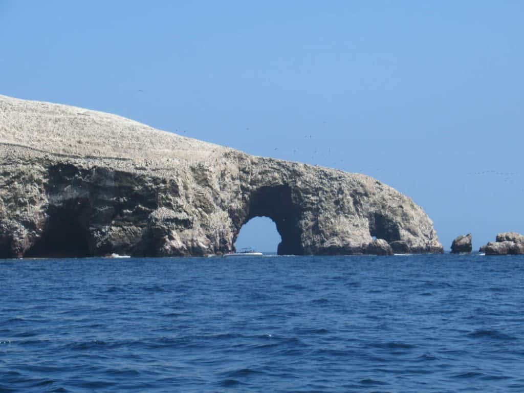 The iconic rock formations of Paracas National Reserve in Peru, where a large rock arch juts out over the blue ocean waters, creating a striking natural scene that is one of the must-see places to visit in Peru.