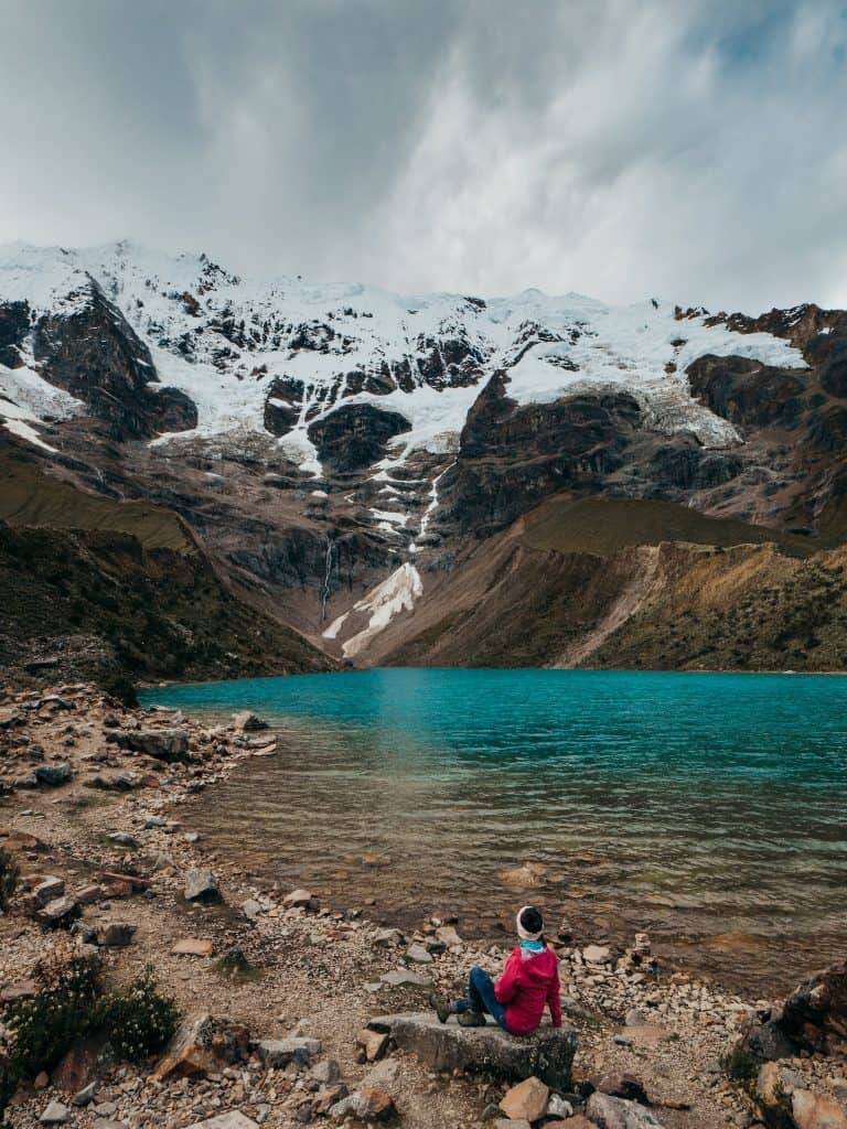 Me sitting by the stunning turquoise waters of Humantay Lake, surrounded by towering snow-capped mountains, a breathtaking spot that is one of the incredible places to visit in Peru.