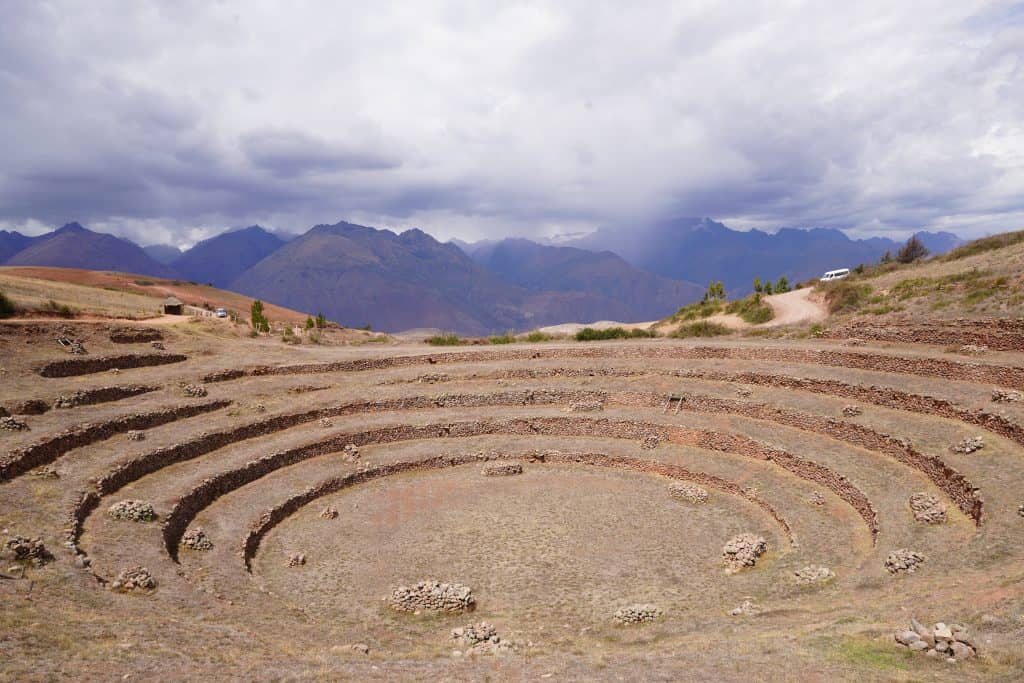 The circular terraced depressions of Moray, an archaeological site in Peru, surrounded by mountains under a cloudy sky, highlighting one of the unique places to visit in Peru.