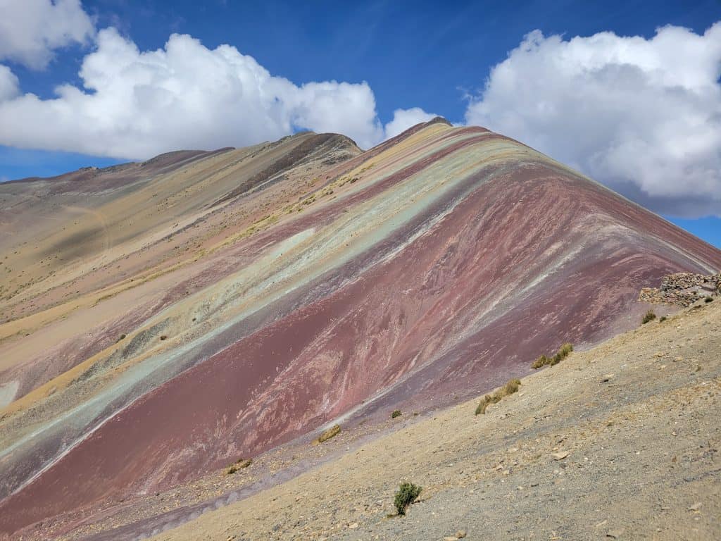 Stunning Rainbow Mountain, or Vinicunca, in Peru. The mountain's vibrant stripes of red, yellow, green, and blue create a breathtaking view under the clear blue sky, making it one of the must-see places to visit in Peru.