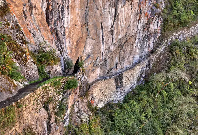 The narrow and dramatic Inca Bridge at Machu Picchu, constructed along a steep cliff face. Visiting this bridge is one of the thrilling things to do at Machu Picchu. The pathway, carved directly into the rock, is a testament to the creativity and resilience of the ancient builders.