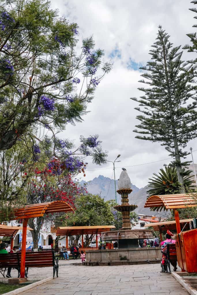 A charming town square in Peru, featuring a central fountain surrounded by lush greenery and flowering trees, with mountains in the background for those looking for peaceful places to visit in Peru.