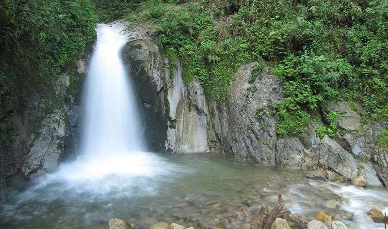 Exploring things to do at Machu Picchu includes visiting the calm waterfall, where the cascading water flows into a clear, rock-strewn pool surrounded by lush green foliage.