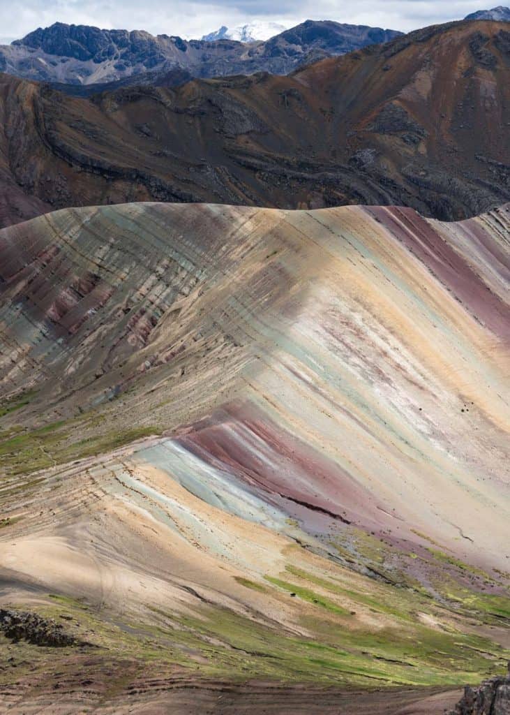 The stunning Rainbow Mountain, one of the must-see places to visit in Peru, featuring vibrant, colorful stripes of red, orange, yellow, and green that ripple across its surface against a backdrop of rugged Andean peaks.