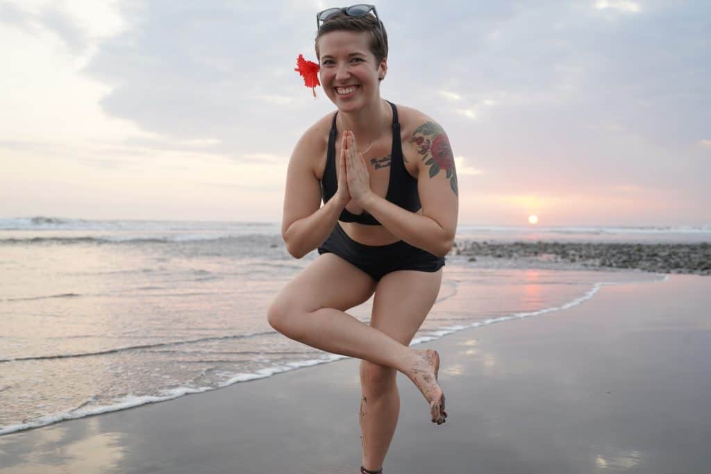 I am balancing in a yoga pose on a peaceful beach in Costa Rica at sunset, with a flower tucked behind my ear, embracing the tranquility and natural beauty that makes Costa Rica day trips so memorable.