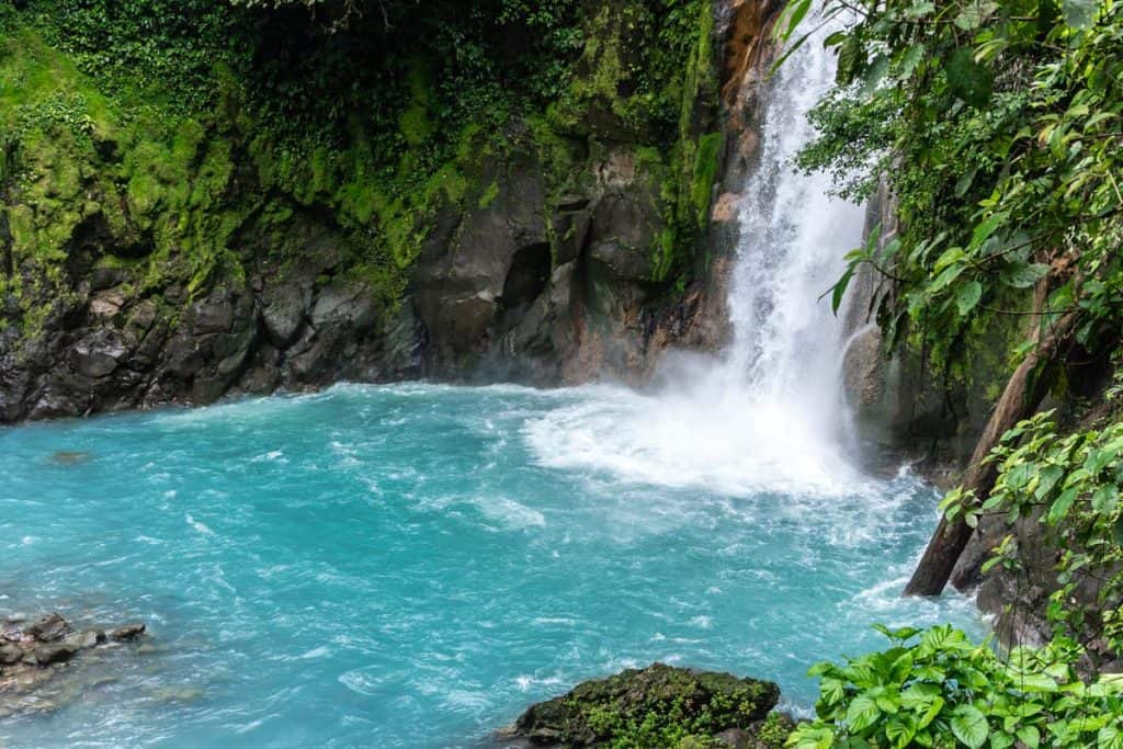 A stunning waterfall cascades into a pool of vibrant turquoise water, surrounded by lush greenery, creating an ideal spot to explore during your Costa Rica day trips.