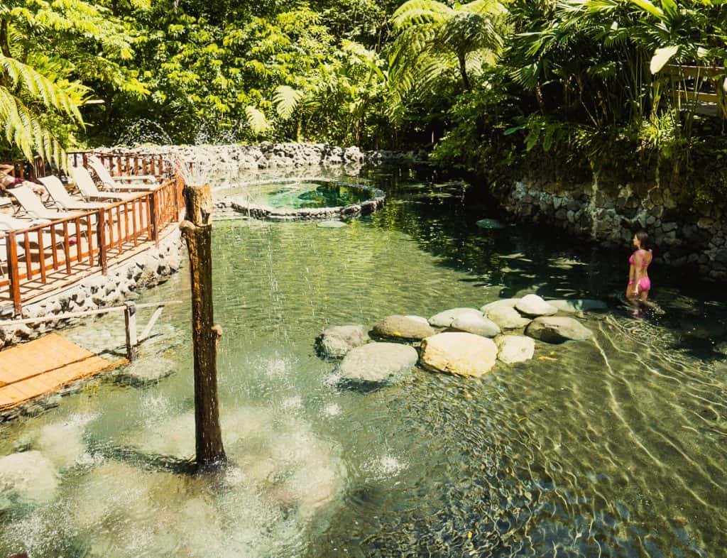 A peaceful hot spring pool with lounge chairs nearby, surrounded by lush tropical greenery, is a perfect spot to unwind during Costa Rica Day Trips.