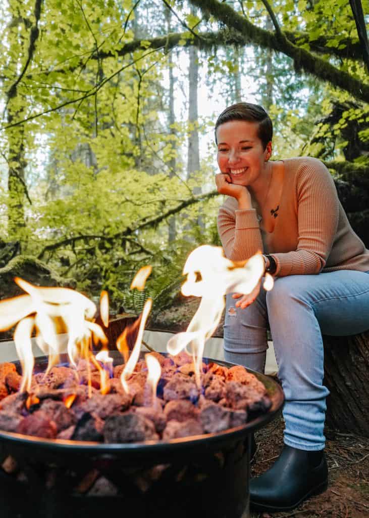 Here I am, enjoying a peaceful moment by the campfire during our glamping in Washington State, sitting on a log and smiling as I watch the flames.