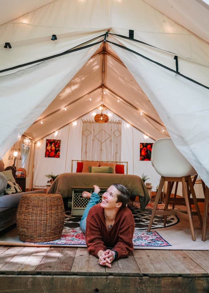 Inside a cozy glamping in Washington State, I am lying on the wooden floor, smiling and enjoying the warm, inviting interior with a comfortable bed, soft lighting, and rustic decor