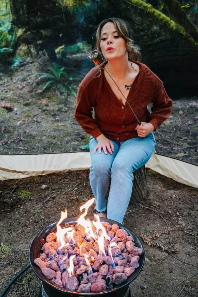 My friend enjoying a cozy evening by the campfire while glamping in Washington State, sitting on a log and roasting marshmallows over the flames.