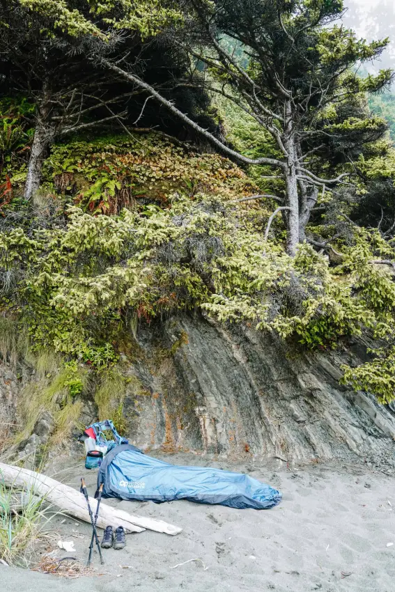 Camping gear and a sleeping bag set up against a rocky hillside at Shi Shi Beach Olympic National Park, surrounded by trees.