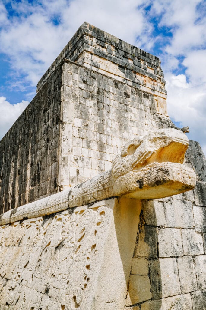 Close-up of a carved stone serpent head on a temple wall at Chichen Itza, captured during Chichen Itza day trips, with blue sky in the background.